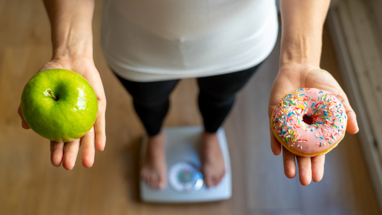 Frau steht mit Apfel und Donut auf der Waage, Copyright Panthermedia