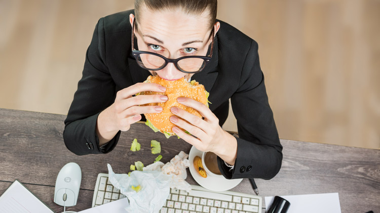 Frau am Schreibtisch isst einen Burger, Copyright Panthermedia