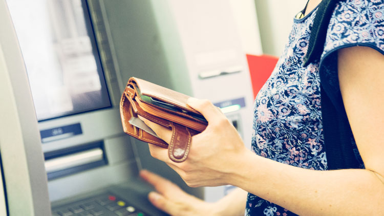 Frau steht mit dem Geldbeutel in der Hand vor Bankautomat, Copyright Panthermedia