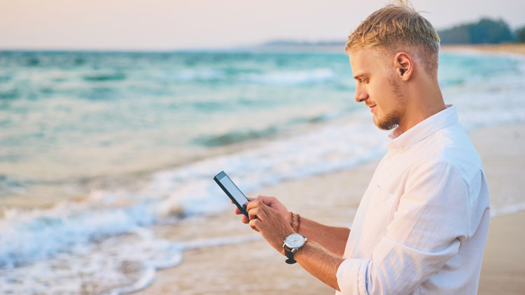 Junger Mann mit Handy am Strand in der Abendsonne, Copyright Panthermedia